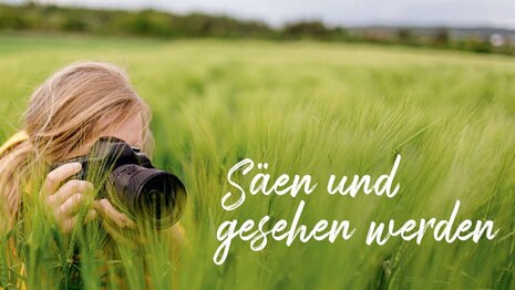 Fotowettbewerb »Mein grüner Traumberuf«: Foto einer Person, die mit einer Kamera inmitten von einem Getreidefeld sitzt, daneben der Schriftzug »Säen und gesehen werden«
